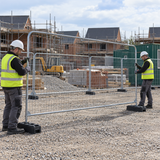 Two workers installing an Eco Heras fence panel into rubber feet